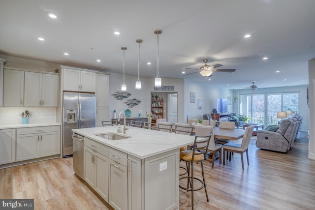 kitchen with light wood-type flooring, white cabinetry, a center island with sink, sink, and ceiling fan