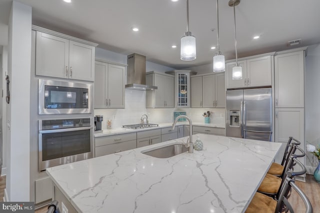 kitchen with decorative light fixtures, appliances with stainless steel finishes, wall chimney range hood, and tasteful backsplash