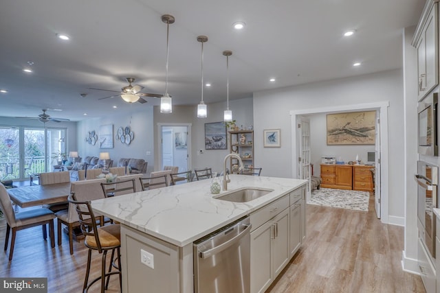 kitchen with appliances with stainless steel finishes, ceiling fan, sink, light wood-type flooring, and a kitchen island with sink