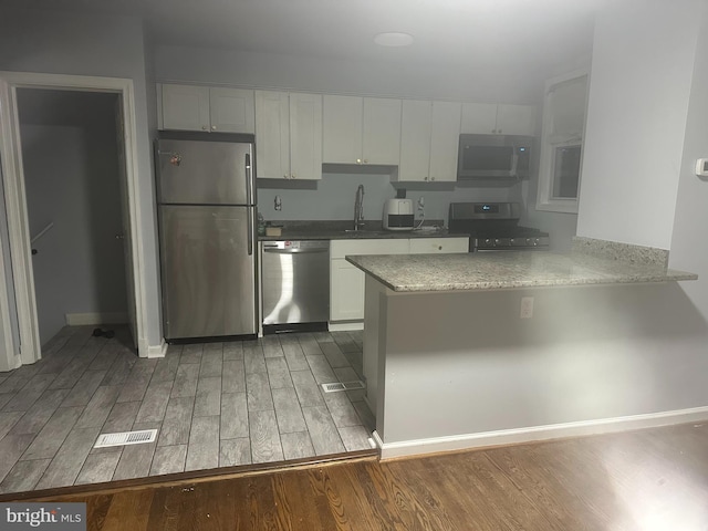 kitchen featuring white cabinetry, appliances with stainless steel finishes, kitchen peninsula, and hardwood / wood-style floors