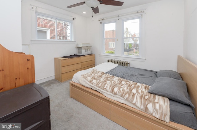 bedroom featuring light colored carpet, multiple windows, ceiling fan, and radiator heating unit