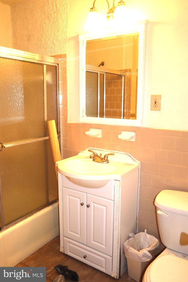 full bathroom featuring bath / shower combo with glass door, tile walls, backsplash, vanity, and toilet