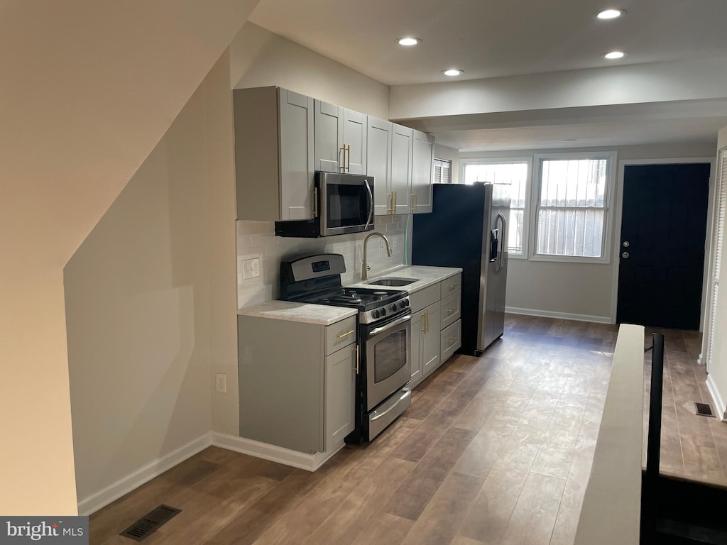 kitchen with wood-type flooring, gray cabinetry, appliances with stainless steel finishes, sink, and tasteful backsplash