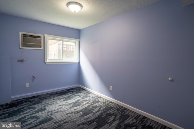 unfurnished room featuring a wall unit AC, dark carpet, and a textured ceiling