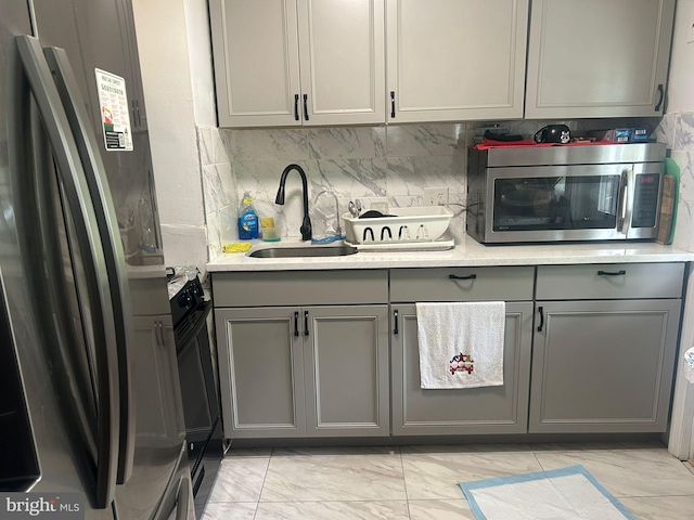 kitchen with gray cabinets, stainless steel appliances, tasteful backsplash, sink, and light tile floors