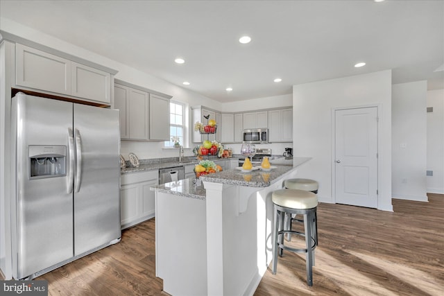 kitchen with dark wood-type flooring, stainless steel appliances, light stone counters, a kitchen bar, and a kitchen island