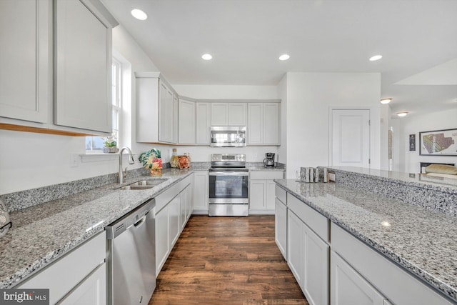 kitchen with light stone countertops, appliances with stainless steel finishes, dark wood-type flooring, sink, and white cabinets