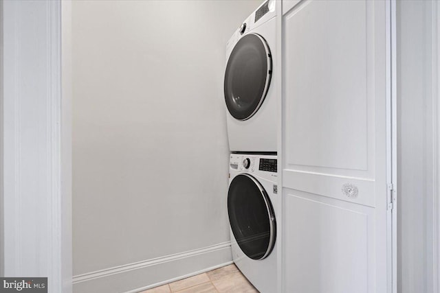 clothes washing area featuring light tile patterned floors and stacked washer and clothes dryer