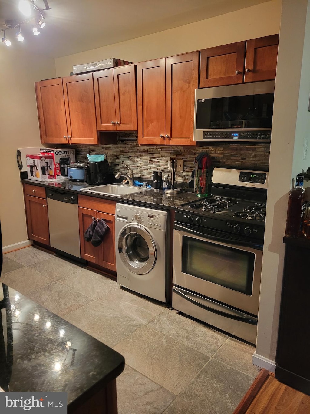 kitchen featuring light tile flooring, appliances with stainless steel finishes, sink, tasteful backsplash, and washer / dryer