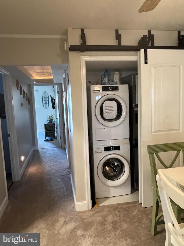 laundry room featuring stacked washer and dryer, a barn door, and carpet flooring