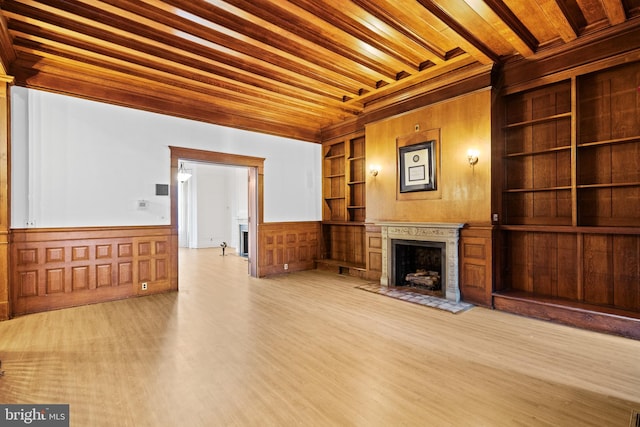 unfurnished living room with beam ceiling, built in shelves, wood walls, and light wood-type flooring