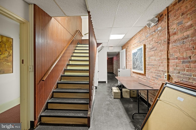 staircase featuring brick wall, wood walls, and a paneled ceiling