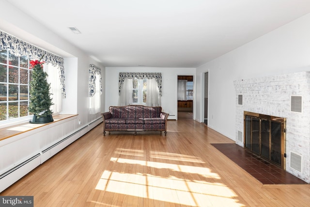 living room featuring hardwood / wood-style flooring, baseboard heating, and a brick fireplace