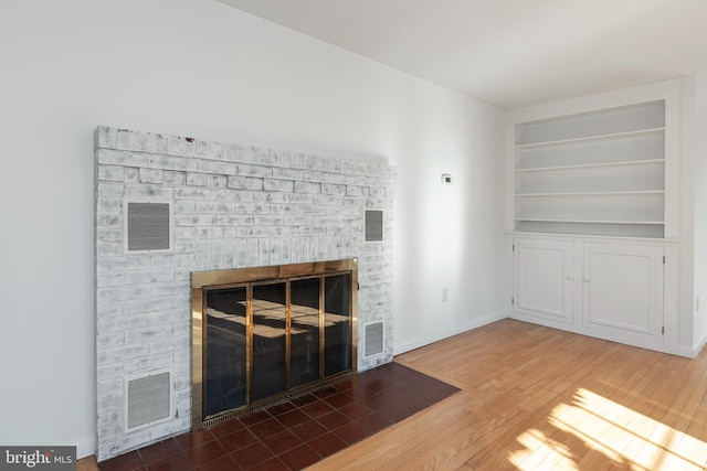 unfurnished living room with hardwood / wood-style flooring, built in shelves, and a fireplace