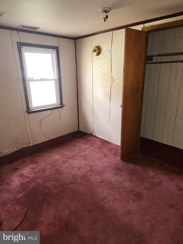 unfurnished bedroom featuring wooden walls, carpet, and a closet