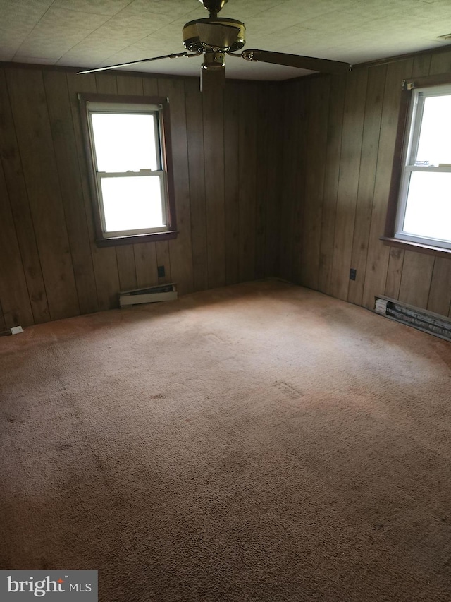 empty room with wood walls, ceiling fan, carpet, and a baseboard heating unit