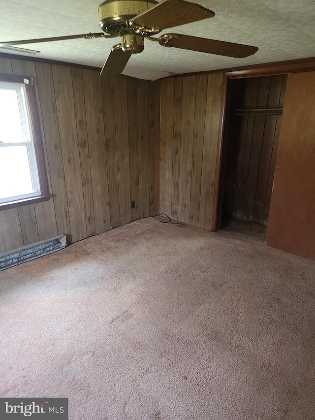 empty room with wooden walls, carpet flooring, a baseboard heating unit, and ceiling fan