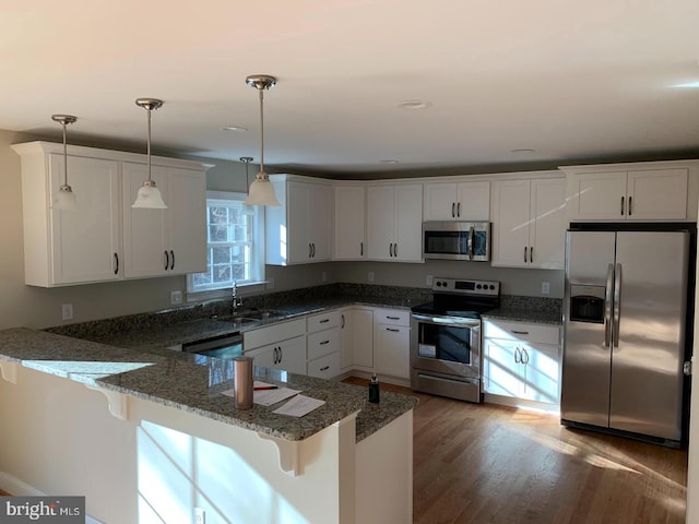 kitchen featuring appliances with stainless steel finishes, decorative light fixtures, white cabinets, a kitchen bar, and kitchen peninsula