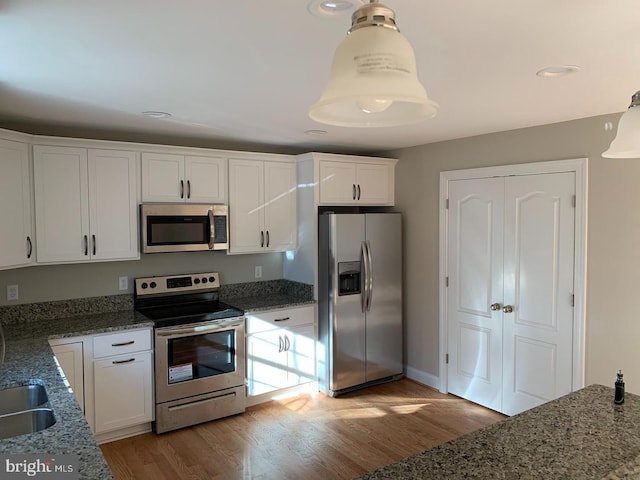 kitchen with stainless steel appliances, hanging light fixtures, white cabinets, and light hardwood / wood-style flooring