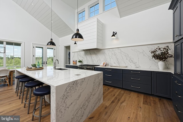 kitchen featuring a kitchen island with sink, sink, high vaulted ceiling, stainless steel stove, and a breakfast bar area