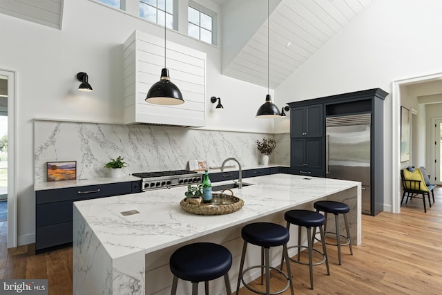 kitchen with a kitchen breakfast bar, a kitchen island with sink, stainless steel appliances, and high vaulted ceiling