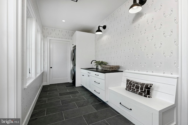 mudroom featuring stacked washer / dryer, sink, and dark tile patterned flooring