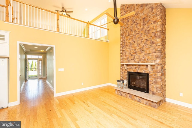 unfurnished living room with a stone fireplace, ceiling fan, hardwood / wood-style floors, and a towering ceiling