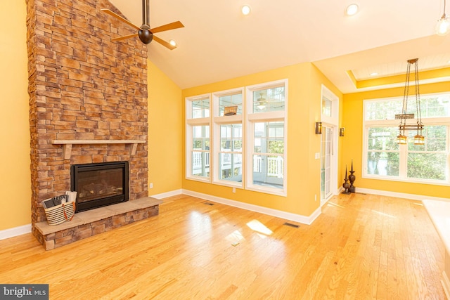 unfurnished living room with hardwood / wood-style floors, vaulted ceiling, a stone fireplace, and ceiling fan