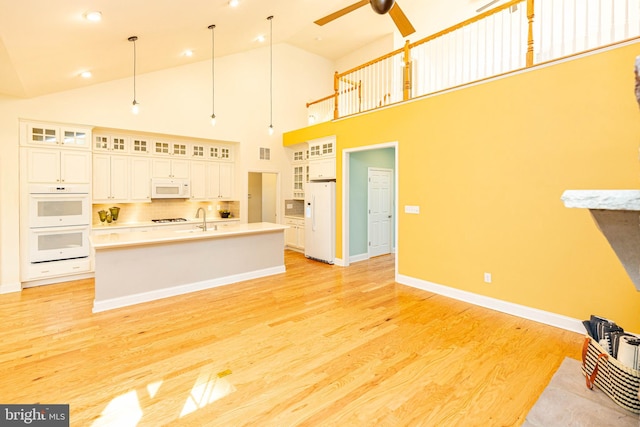 kitchen featuring backsplash, white appliances, light hardwood / wood-style flooring, a high ceiling, and an island with sink