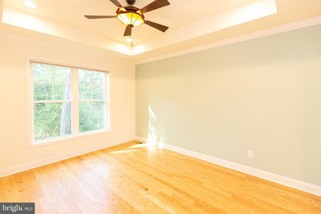 empty room featuring a tray ceiling, ceiling fan, ornamental molding, and hardwood / wood-style flooring