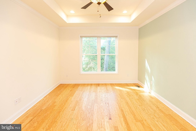 empty room with a tray ceiling, ceiling fan, light hardwood / wood-style floors, and ornamental molding