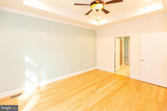 unfurnished room featuring ceiling fan, light hardwood / wood-style floors, a raised ceiling, and crown molding