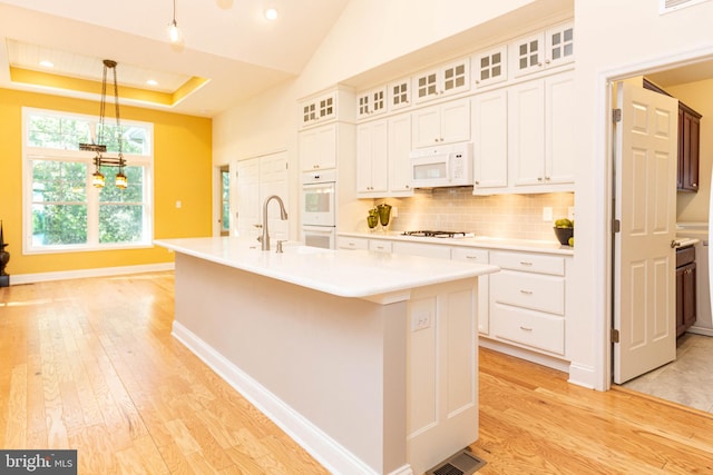 kitchen with backsplash, decorative light fixtures, white appliances, a center island with sink, and white cabinets