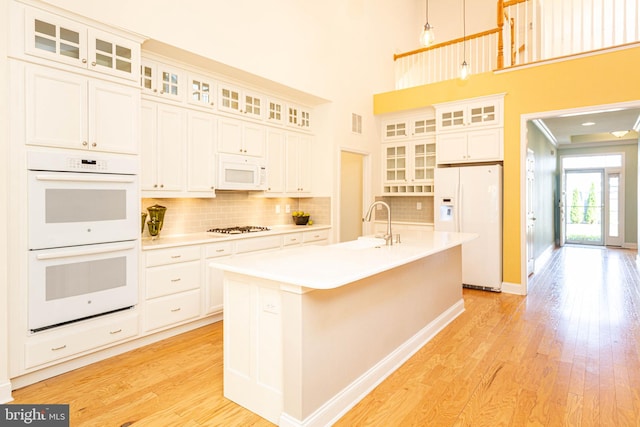 kitchen with backsplash, a kitchen island with sink, white cabinets, and white appliances