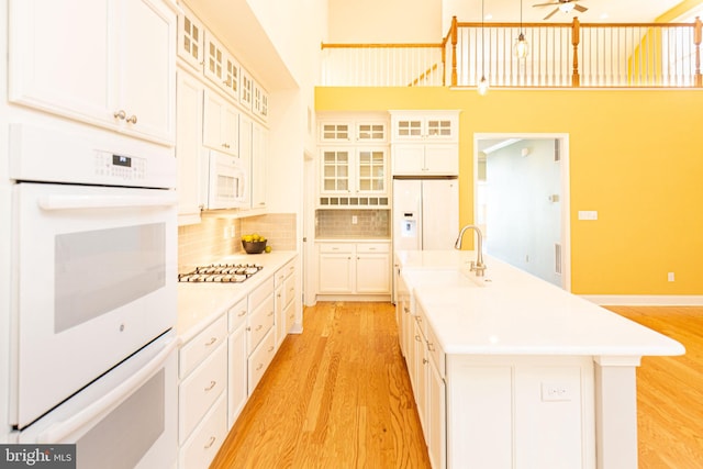 kitchen featuring decorative backsplash, white appliances, sink, white cabinetry, and an island with sink