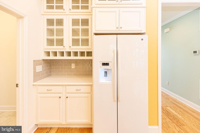 kitchen with white refrigerator with ice dispenser, backsplash, light hardwood / wood-style flooring, and crown molding