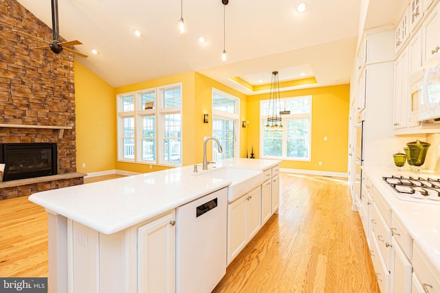 kitchen featuring pendant lighting, white appliances, a kitchen island with sink, sink, and light wood-type flooring