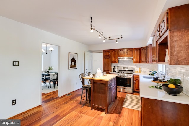 kitchen with gas range, a center island, sink, light hardwood / wood-style flooring, and decorative backsplash