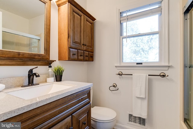 bathroom featuring a shower with door, vanity, and toilet