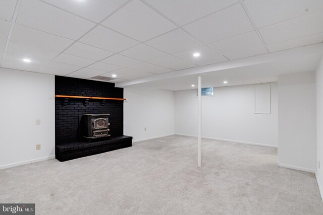 basement featuring carpet flooring, a wood stove, and a drop ceiling