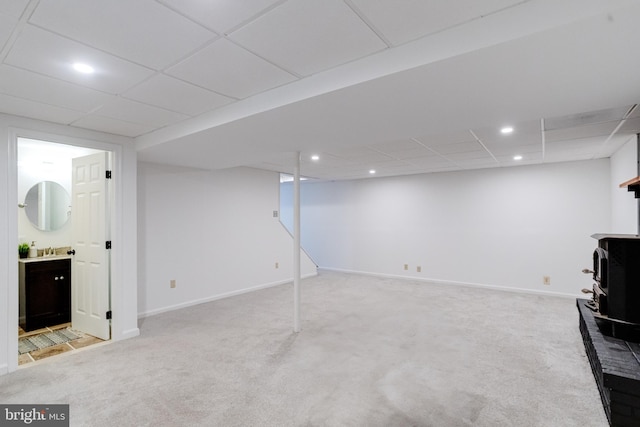 basement with a wood stove, a drop ceiling, and carpet floors