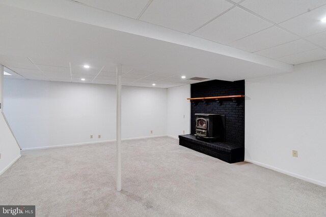 basement featuring carpet, a wood stove, and a drop ceiling