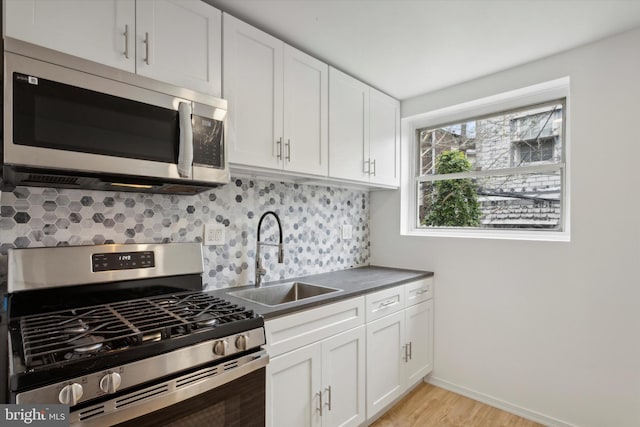 kitchen with backsplash, stainless steel appliances, light hardwood / wood-style floors, white cabinets, and sink