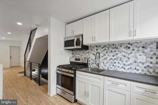 kitchen with white cabinets, light hardwood / wood-style flooring, appliances with stainless steel finishes, sink, and tasteful backsplash