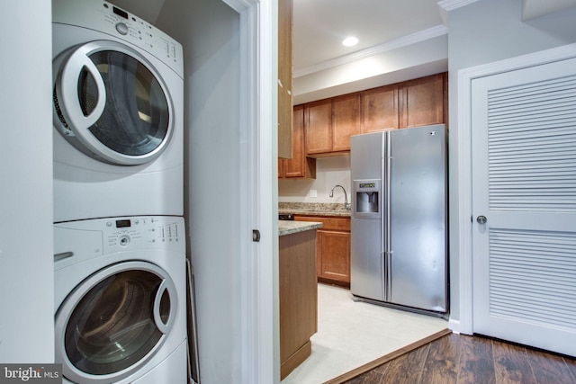 clothes washing area featuring wood-type flooring, sink, stacked washer / dryer, and ornamental molding