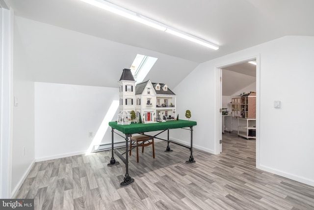 playroom featuring a baseboard heating unit, light wood-type flooring, and vaulted ceiling with skylight