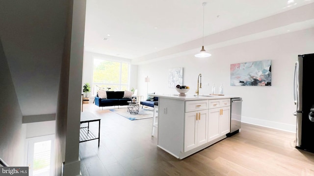 kitchen featuring a kitchen island with sink, a breakfast bar area, sink, pendant lighting, and white cabinets