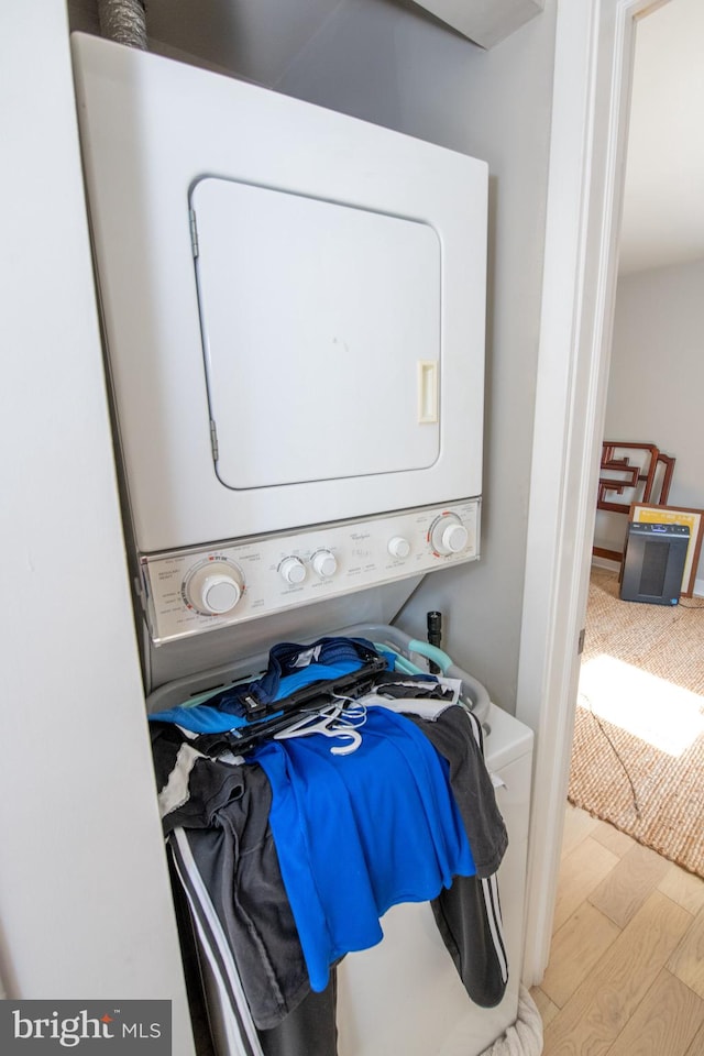 laundry area with light hardwood / wood-style flooring and stacked washing maching and dryer