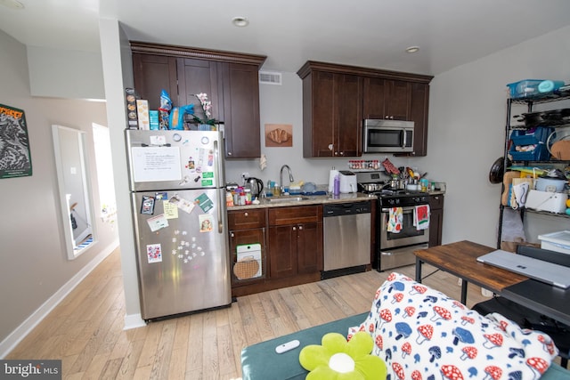 kitchen with dark brown cabinetry, light stone counters, sink, stainless steel appliances, and light hardwood / wood-style flooring