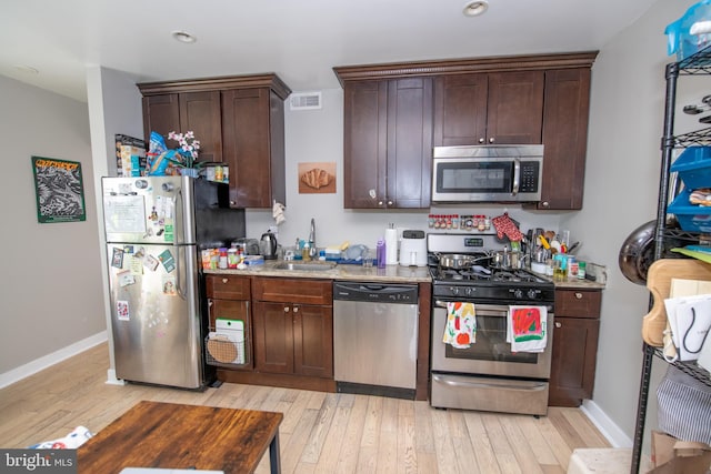 kitchen with light stone counters, stainless steel appliances, sink, and light wood-type flooring